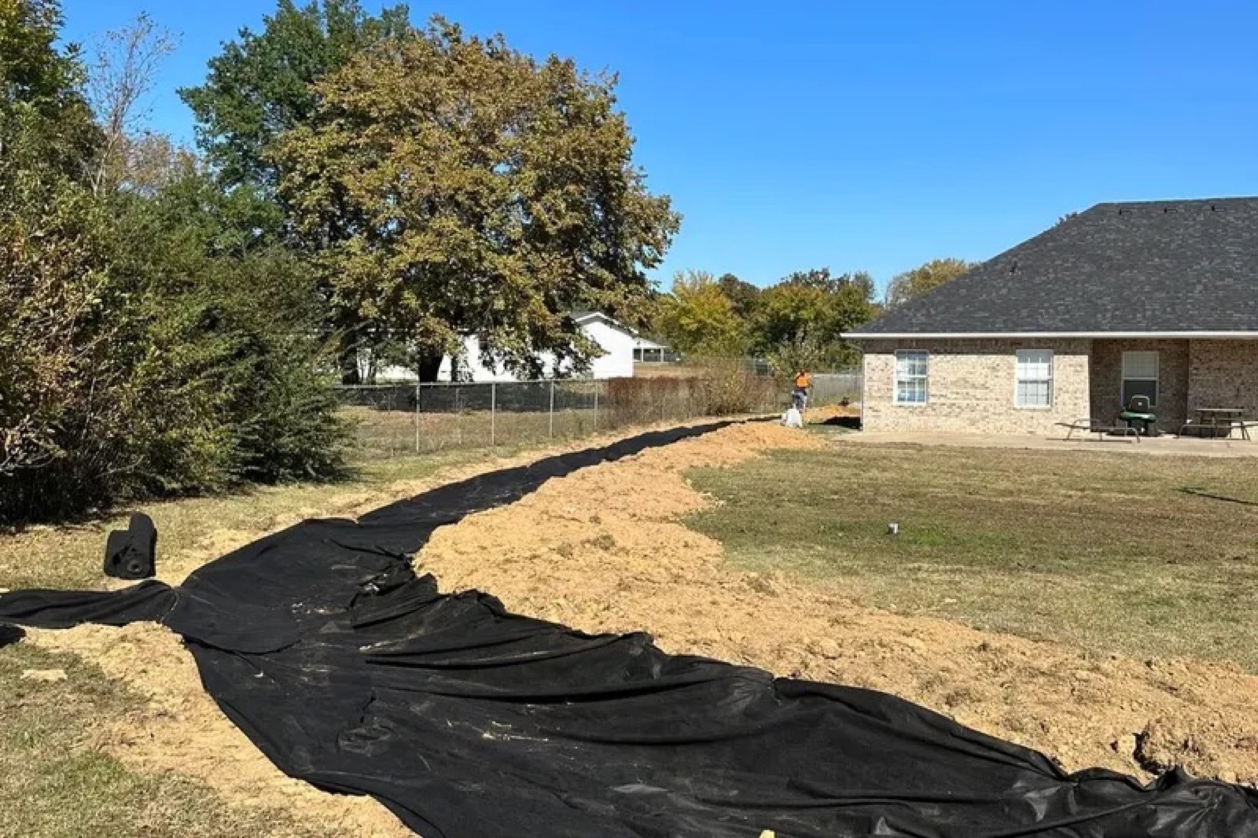 Black erosion-control fabric laid in a trench across a backyard with dirt piled alongside