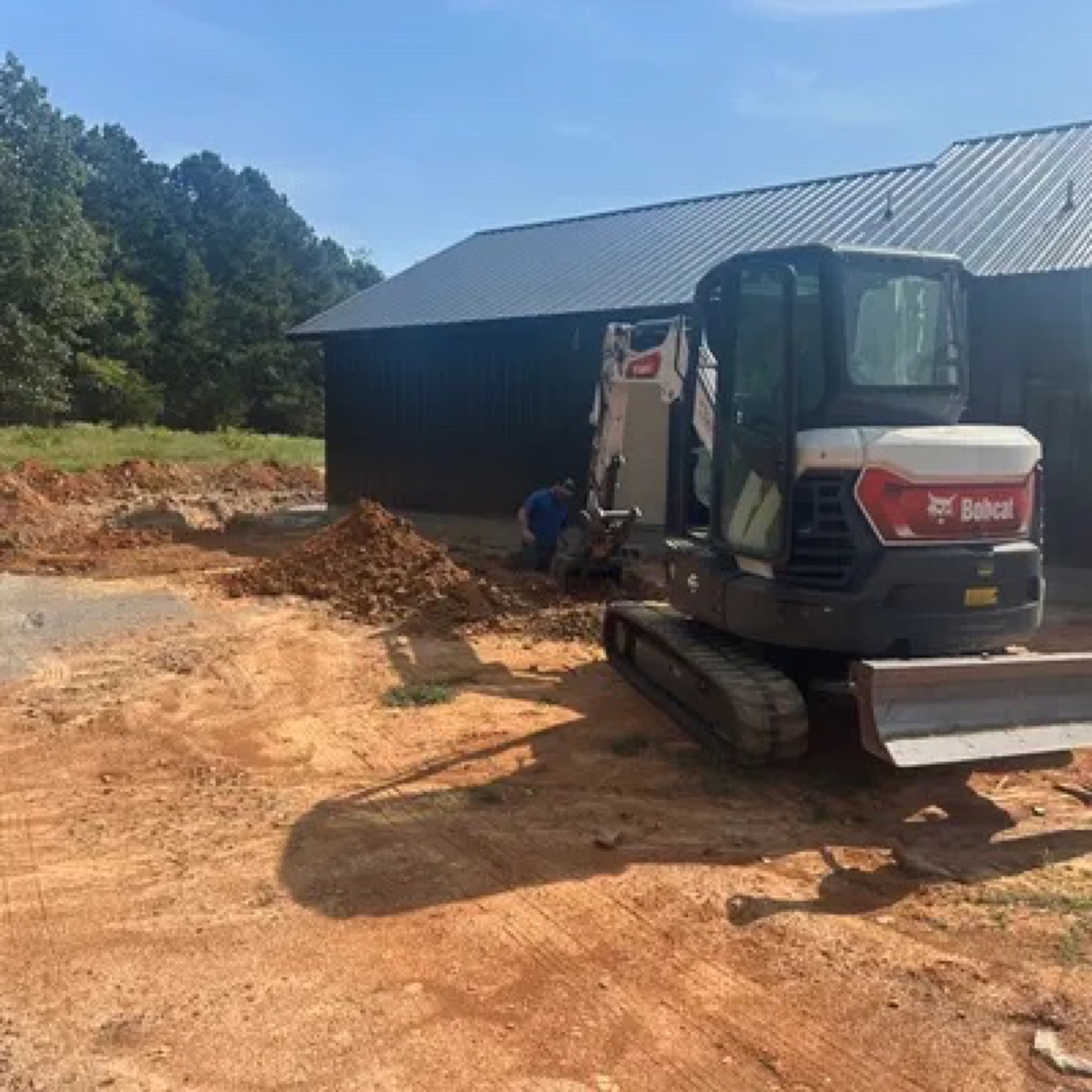 Mini excavator beside a metal barn with dirt piled next to the foundation