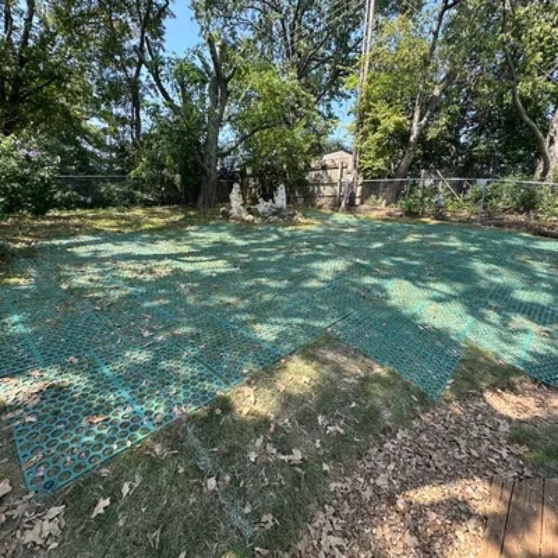 Green plastic ground-stabilization grid laid over a shaded backyard lawn
