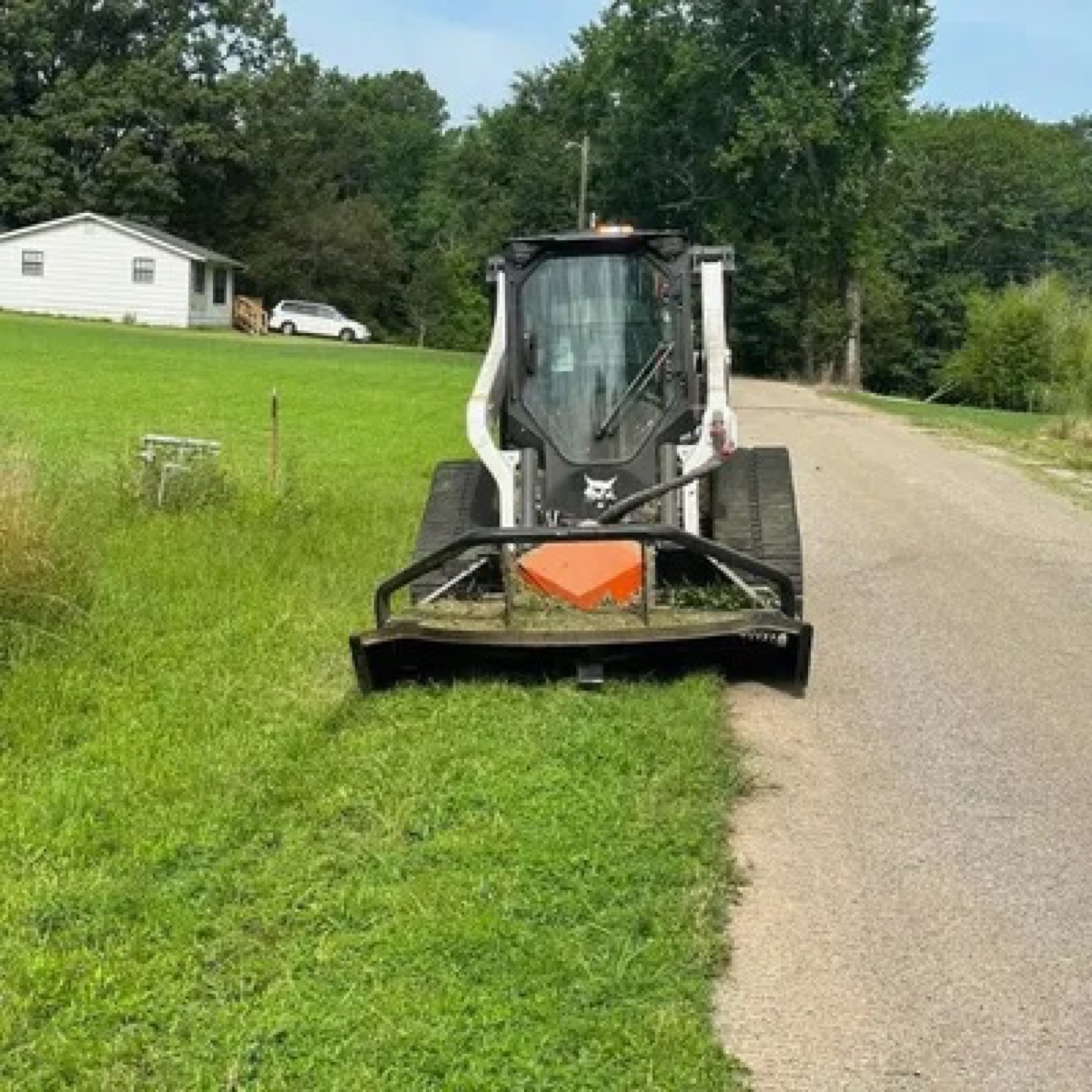 Skid steer mowing tall grass along the edge of a paved road