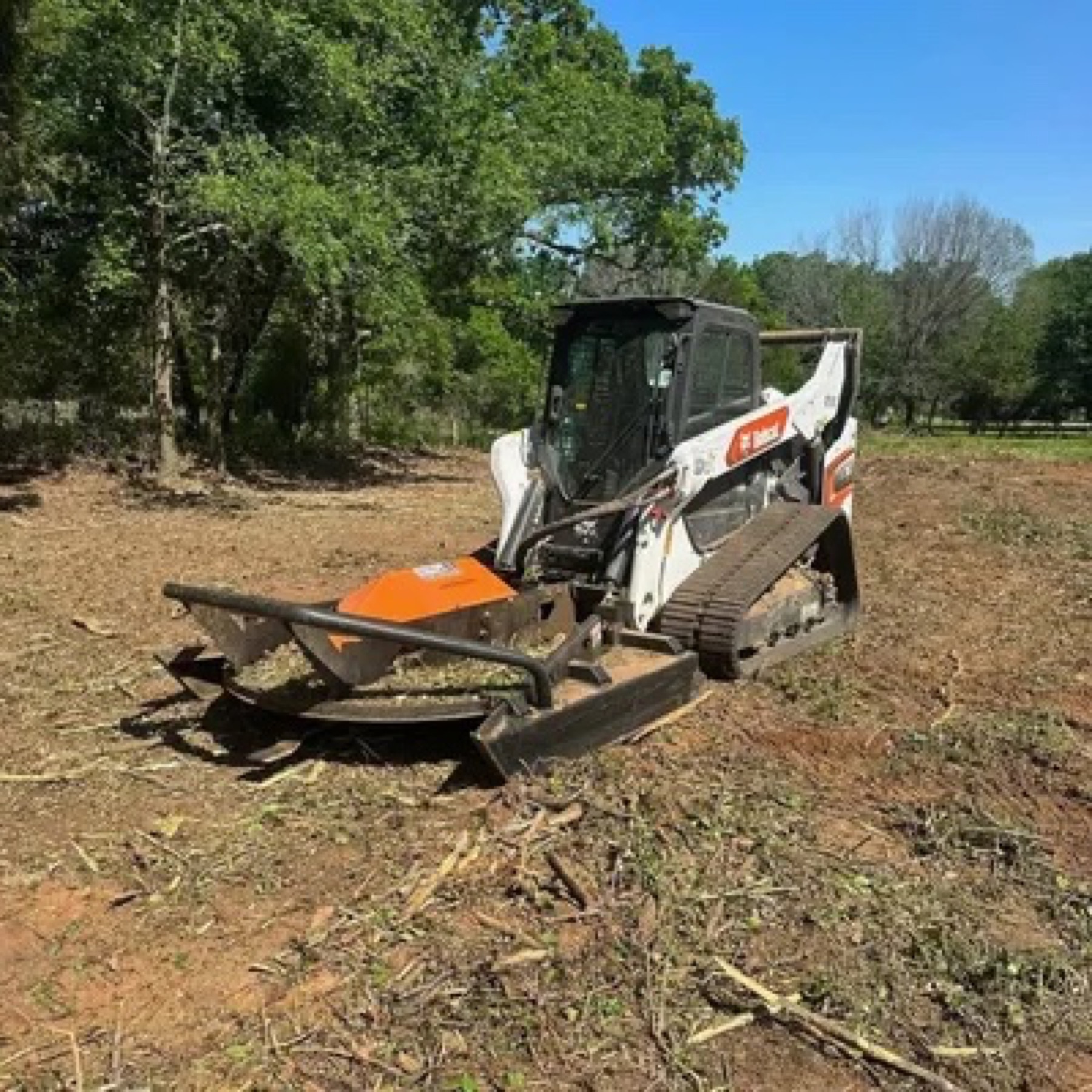 Bobcat with forestry mulcher clearing brush in an open field